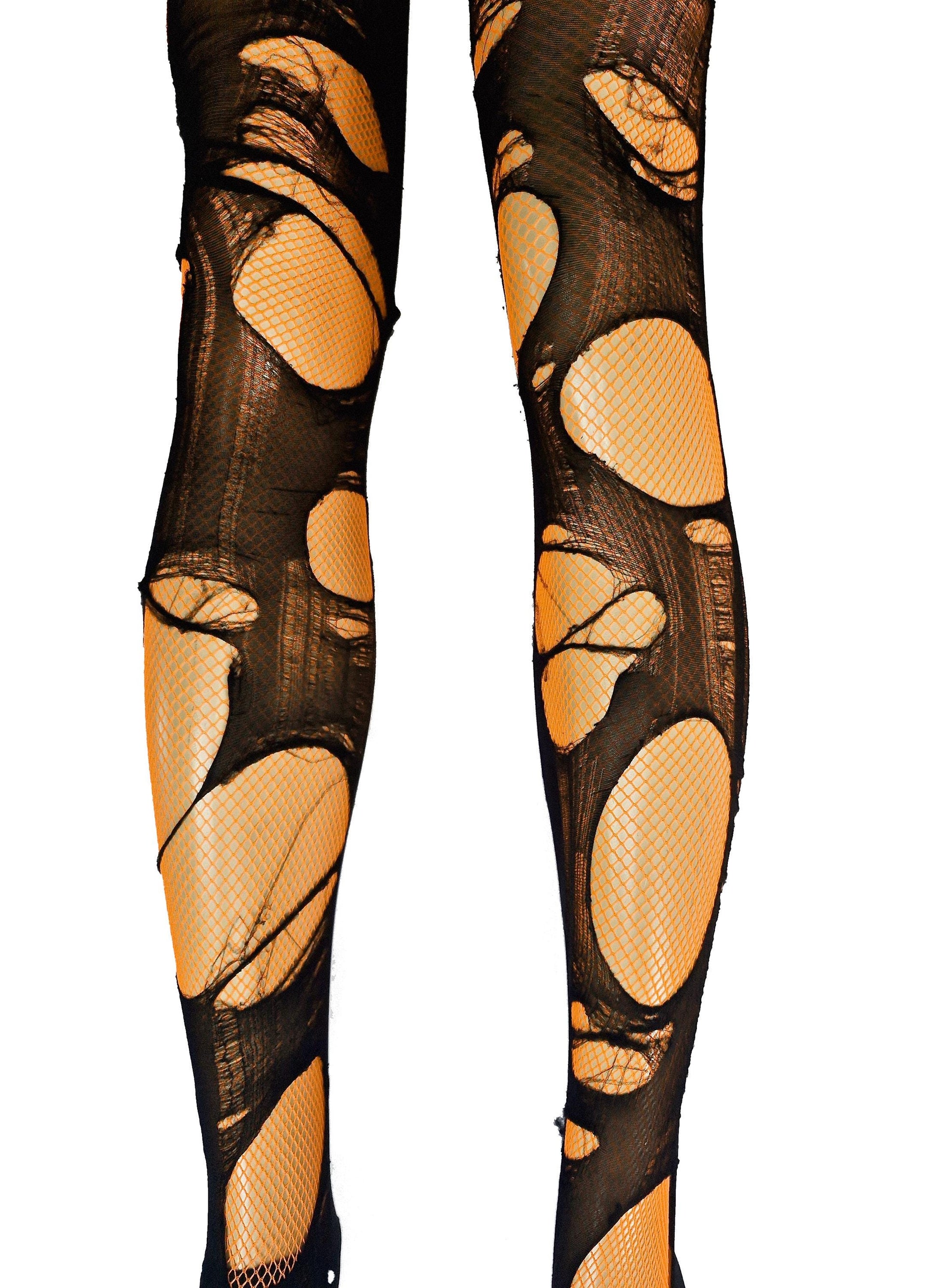 May include: Black ripped fishnet stockings with large holes, revealing an orange underlay. The stockings are designed to create a distressed or edgy look, suitable for costumes or alternative fashion.
